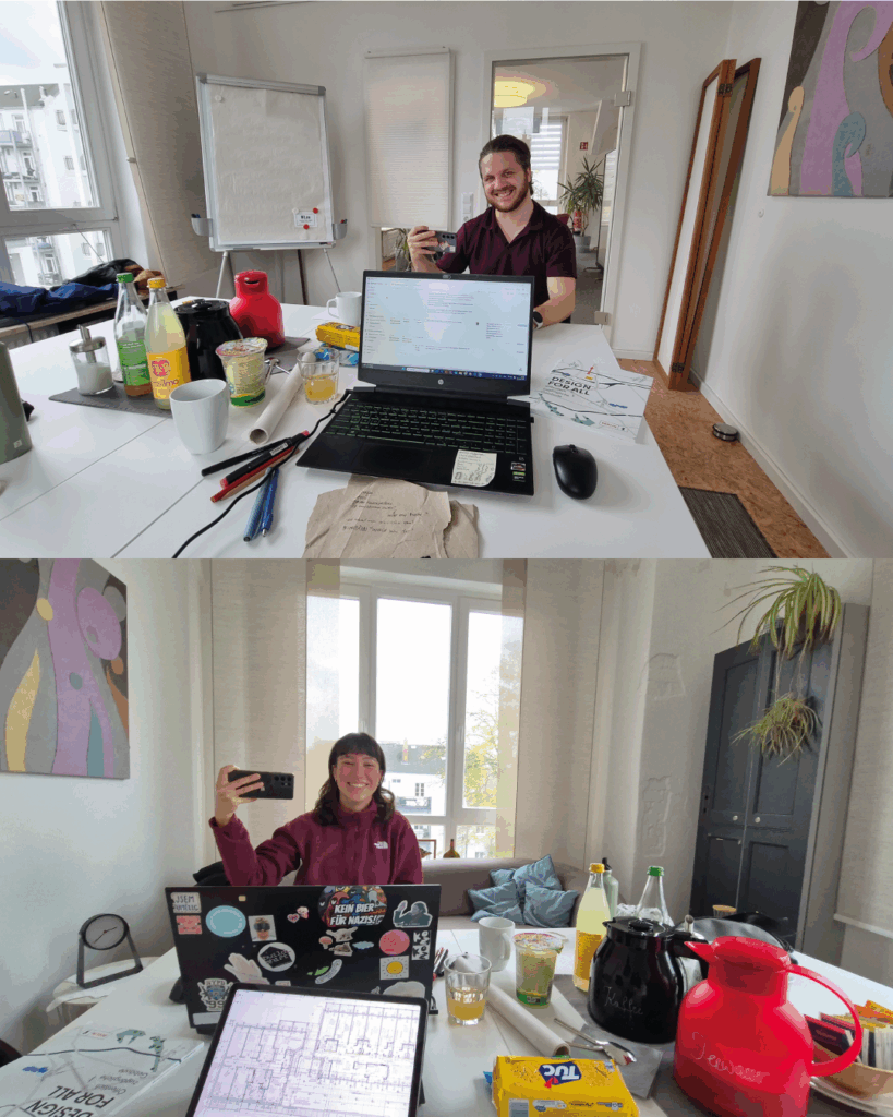 Martin und Slávka von #EineBarriereWeniger gegenüber von einander in einem Coworking-Büro, auf dem Tisch Computer, Stifte und Snacks.